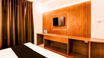 A hotel room with a bed, a TV mounted on a wooden panel, and a small table with a kettle.