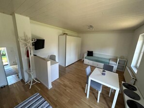A compact living space with a kitchenette, a seating area, and a television mounted on the wall. - 'GardenDream' Charming, quiet little house—near Vienna city center—Vienna (Ebreichsdorf)