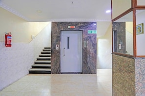 Eine Treppe führt zu einer Tür, über der ein Rauchverbotsschild, ein Brandschutztür-Hinweisschild und ein Feuerlöscher an der Wand angebracht sind.