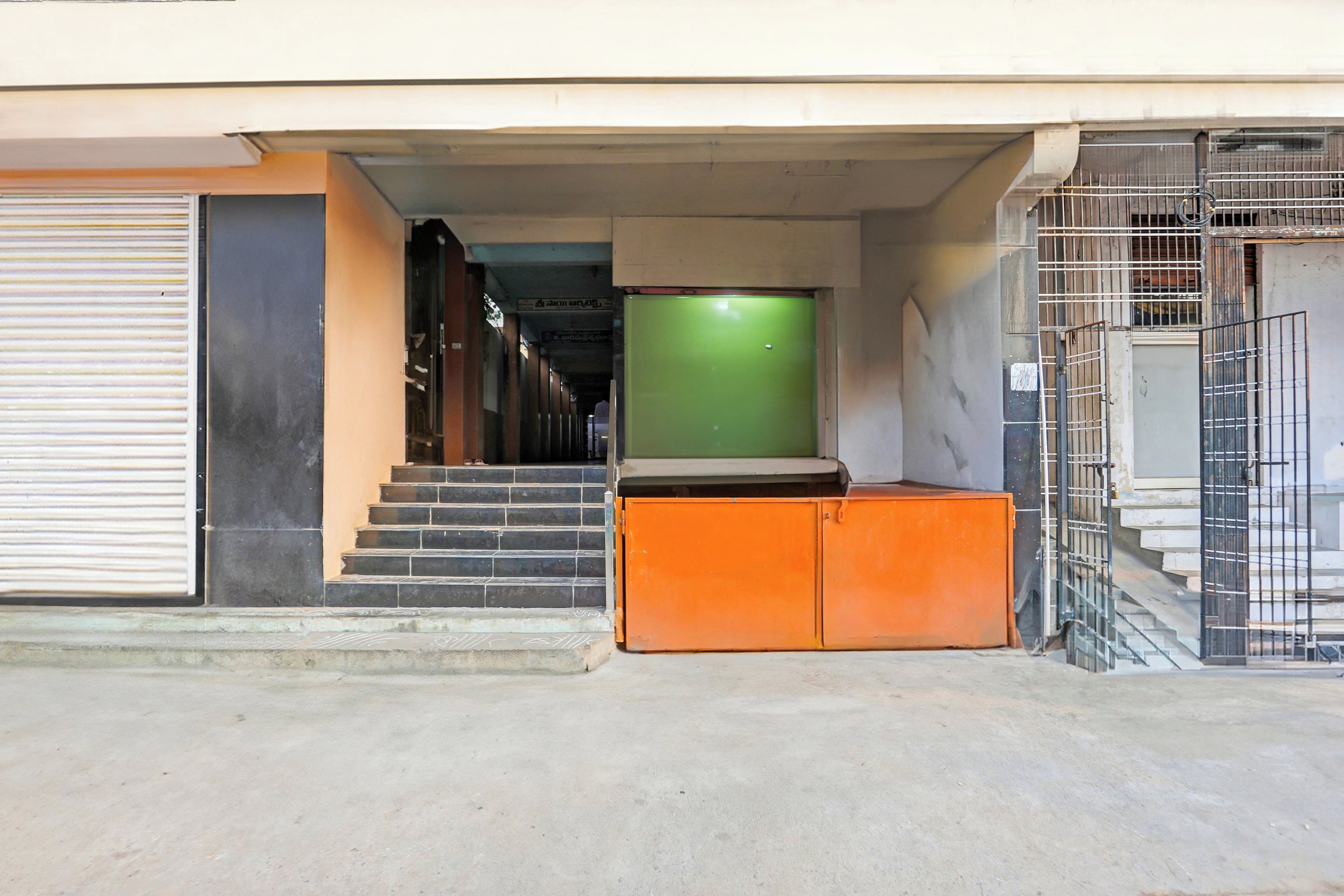 A building entrance with a closed shutter door, a set of stairs leading to a green door, and a metal gate.