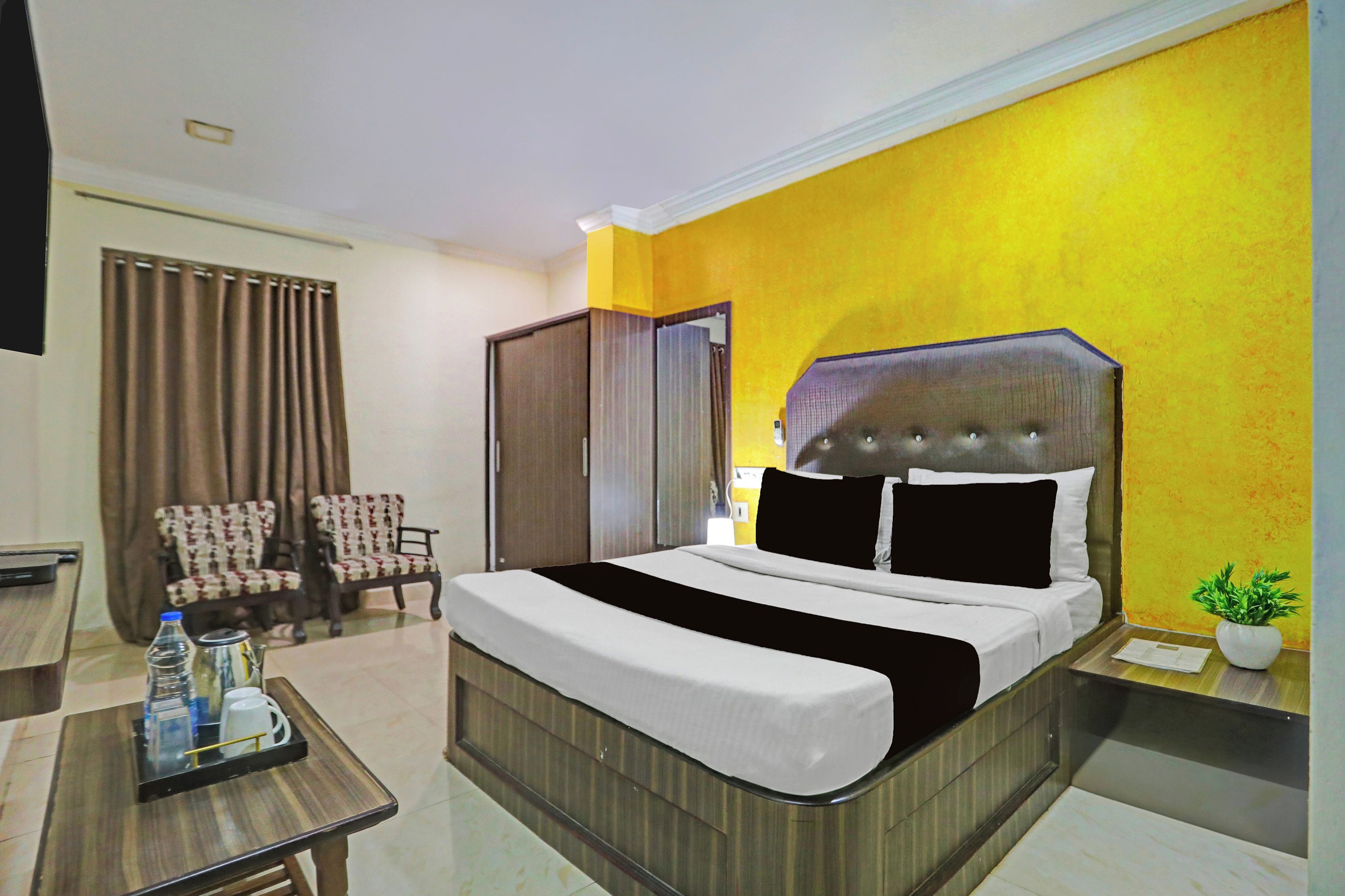 Una habitación de hotel con cama, escritorio, dos sillas, armario y una planta en maceta.