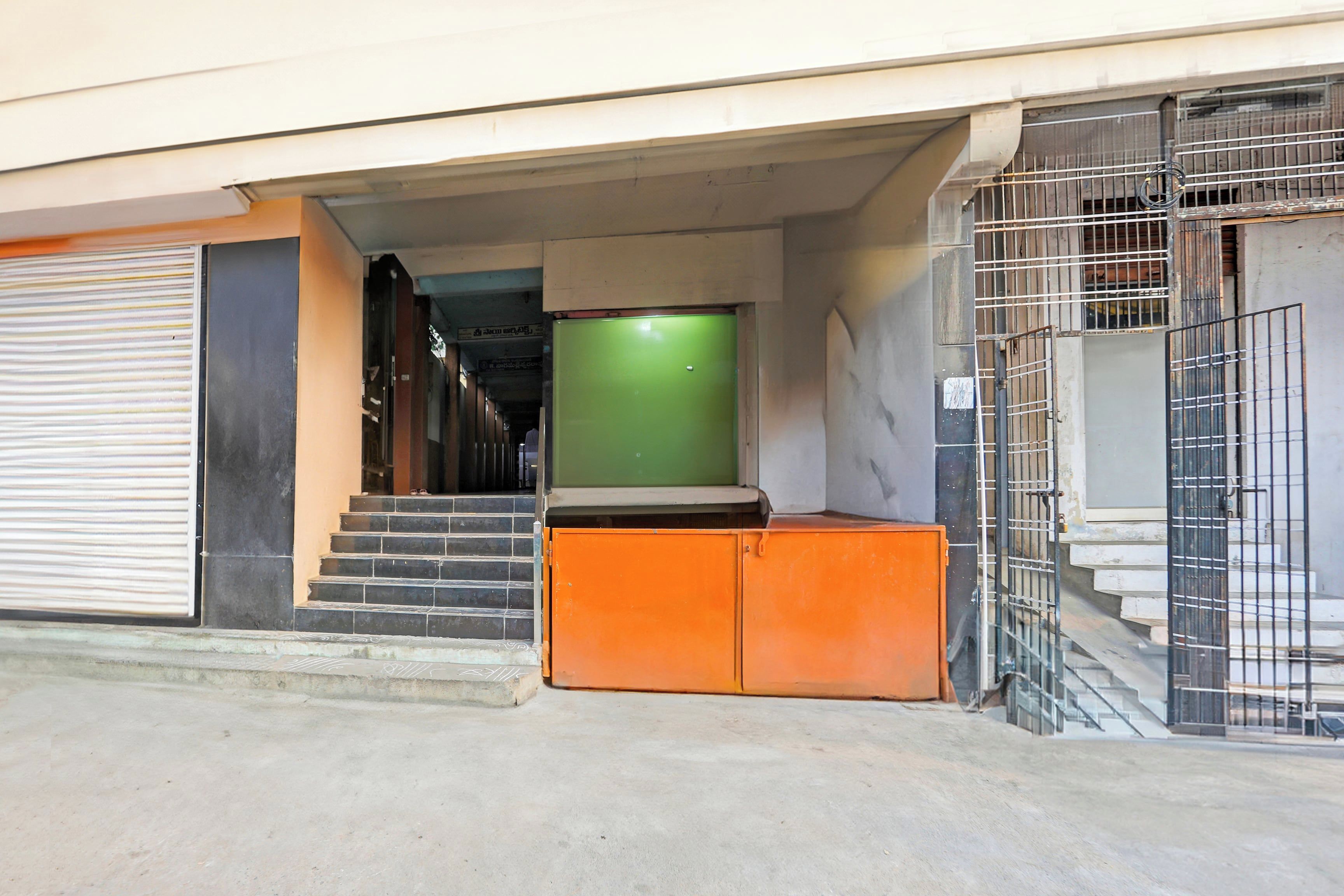 A building entrance with a closed shutter, a staircase leading to an upper level, and a green door.