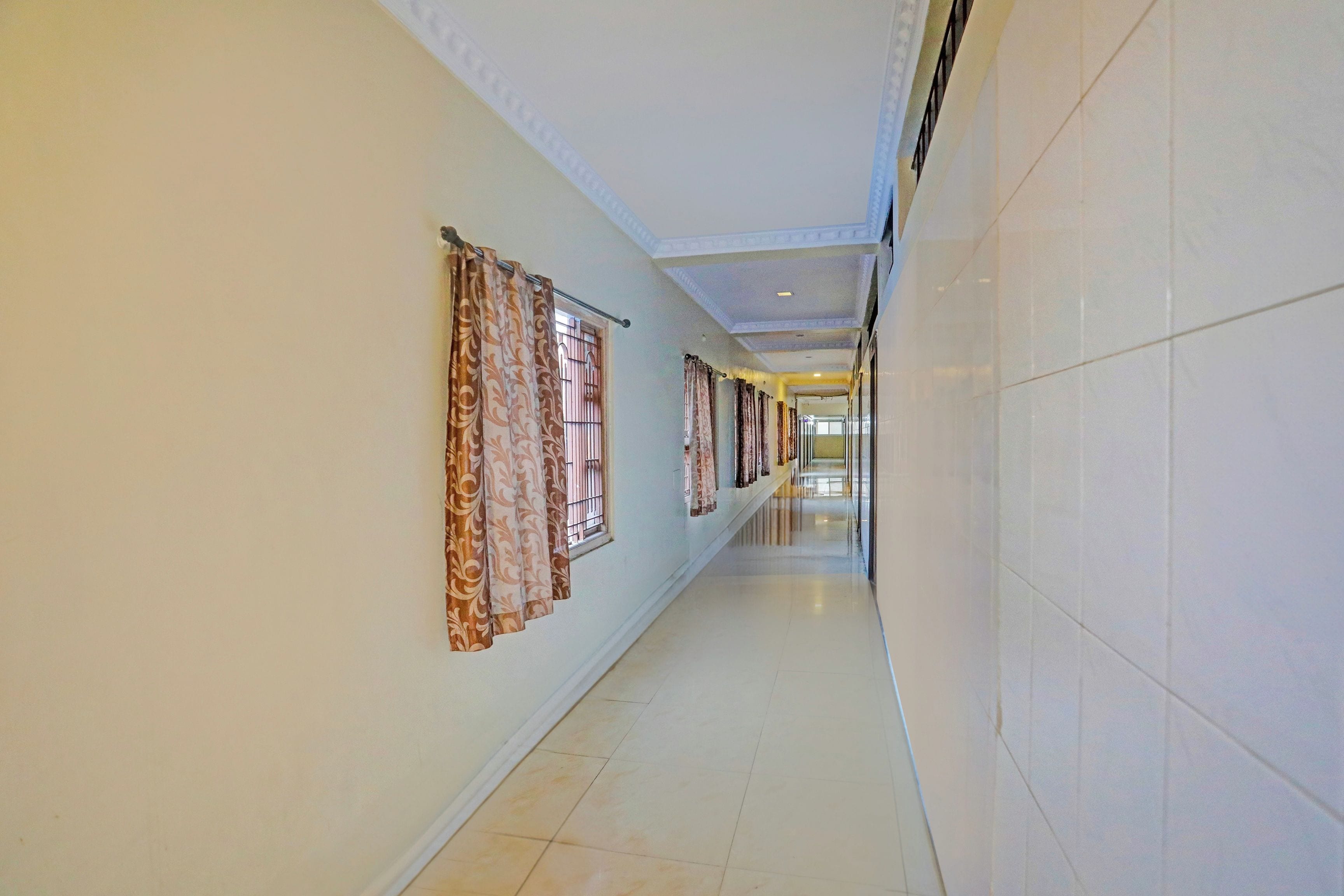 A long, narrow hallway with patterned curtains on the windows, tiled walls, and a tiled floor.