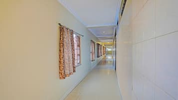 A long, narrow hallway with patterned curtains on the windows, tiled walls, and a tiled floor.