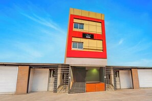 Un edificio de varios pisos con fachada roja y beige, un letrero que indica 'Company Services' y una escalera que conduce a una entrada iluminada en verde.