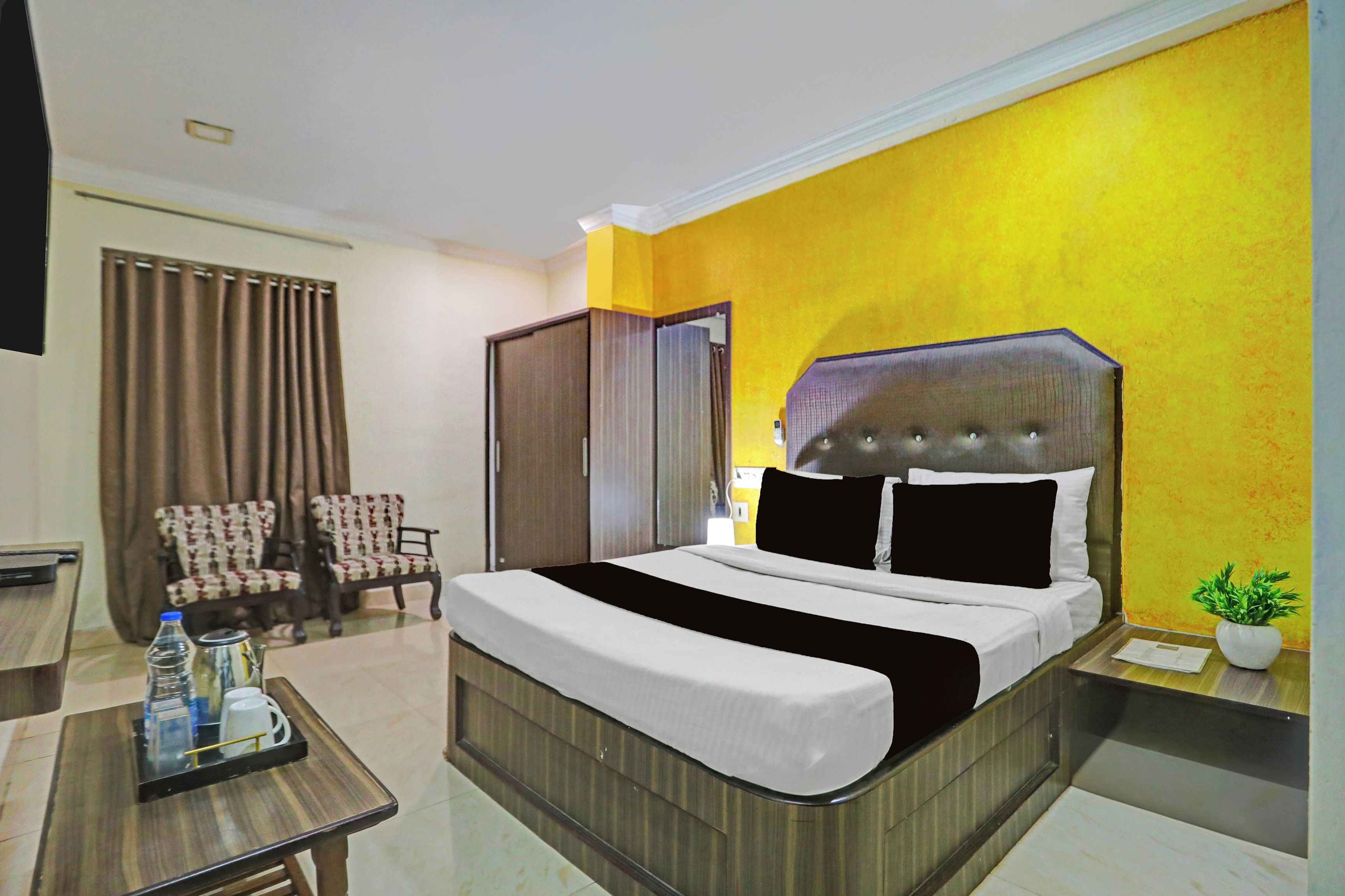 Habitación de hotel con cama, escritorio, dos sillas, armario y planta en maceta.