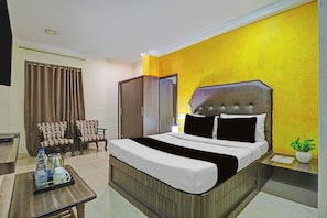 Habitación de hotel con cama, escritorio, dos sillas, armario y planta en maceta.