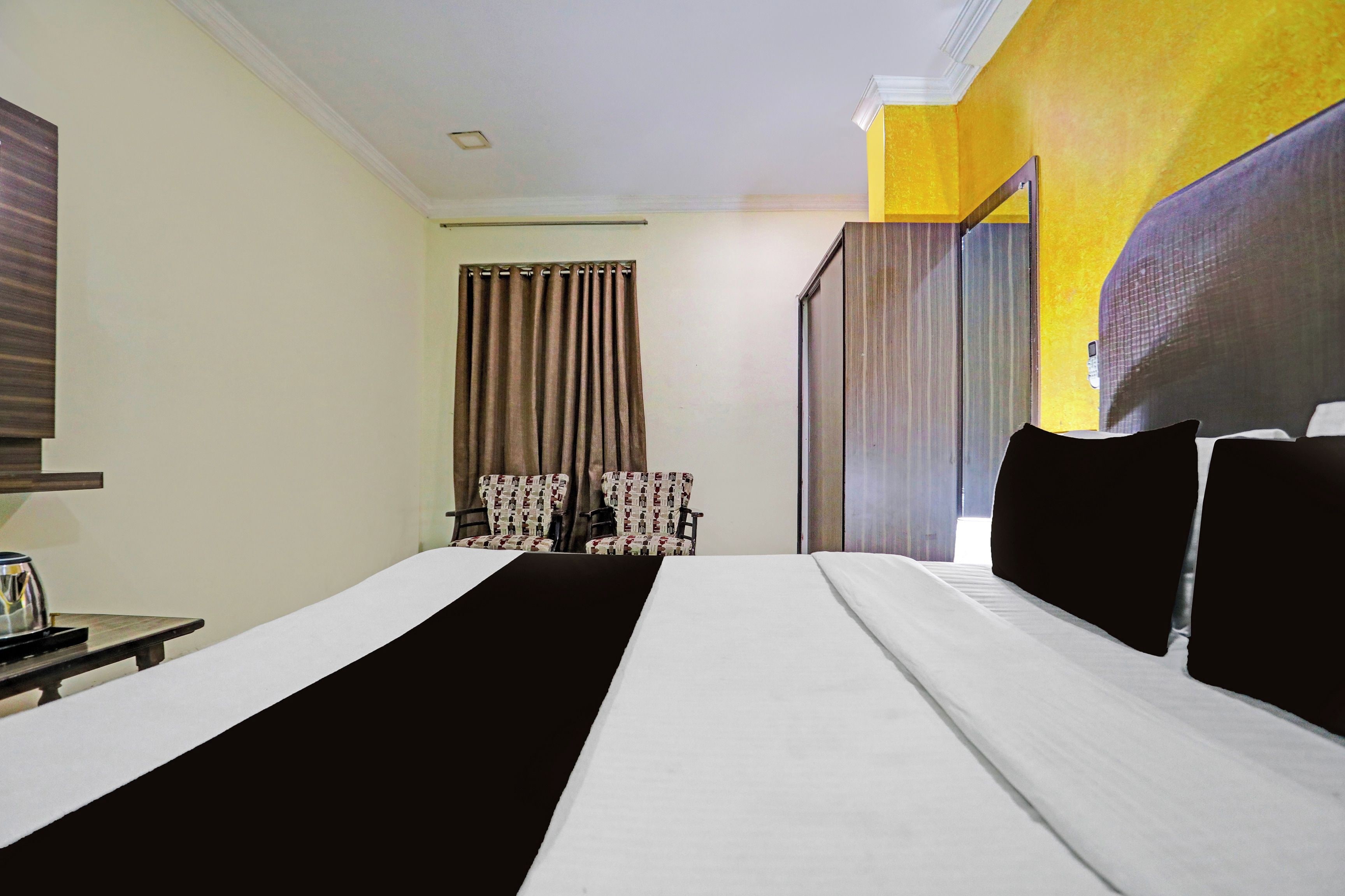 A hotel room with a bed, two chairs, a small table, and a window with curtains.
