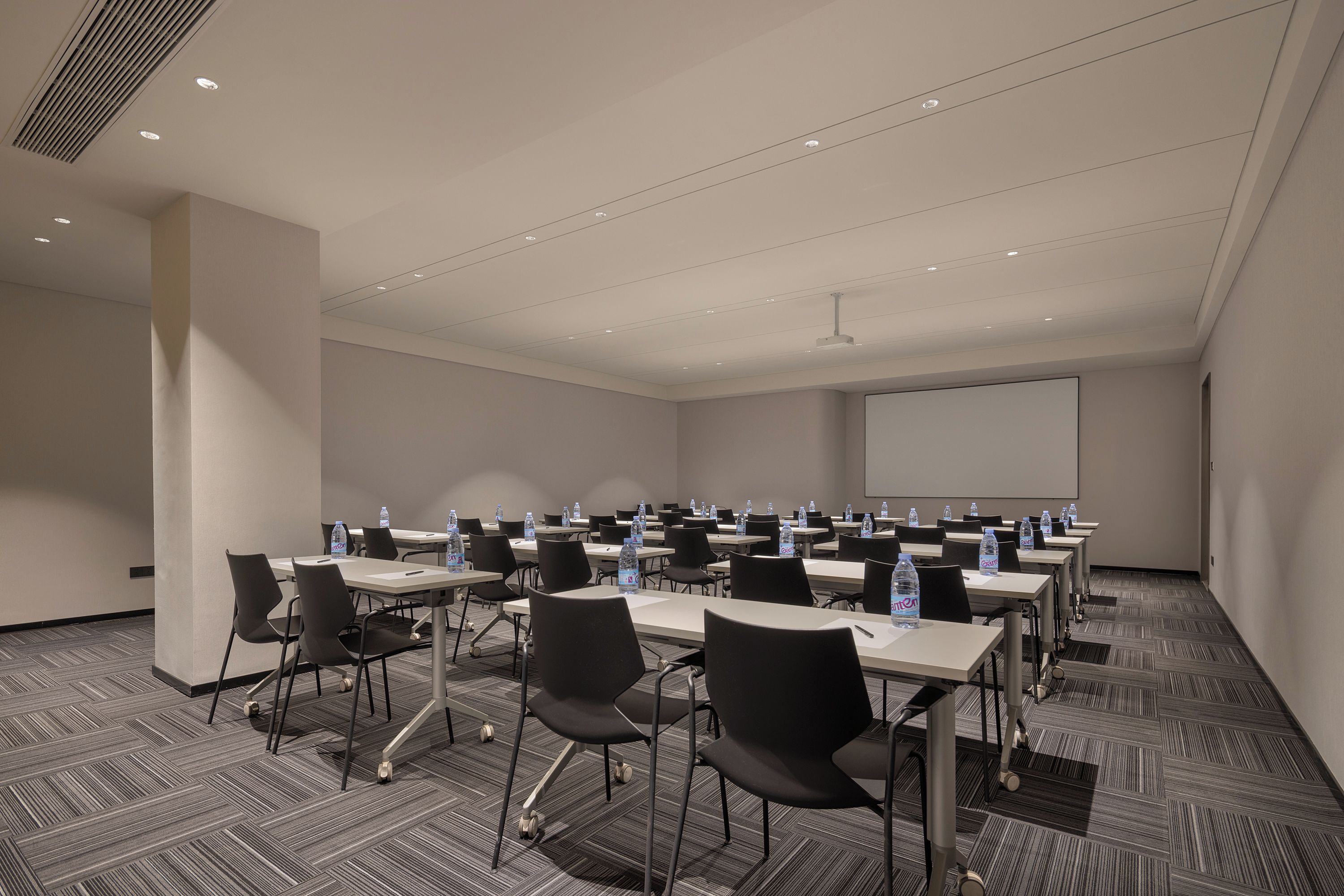 Un salón de conferencias con mesas, sillas y botellas de agua.