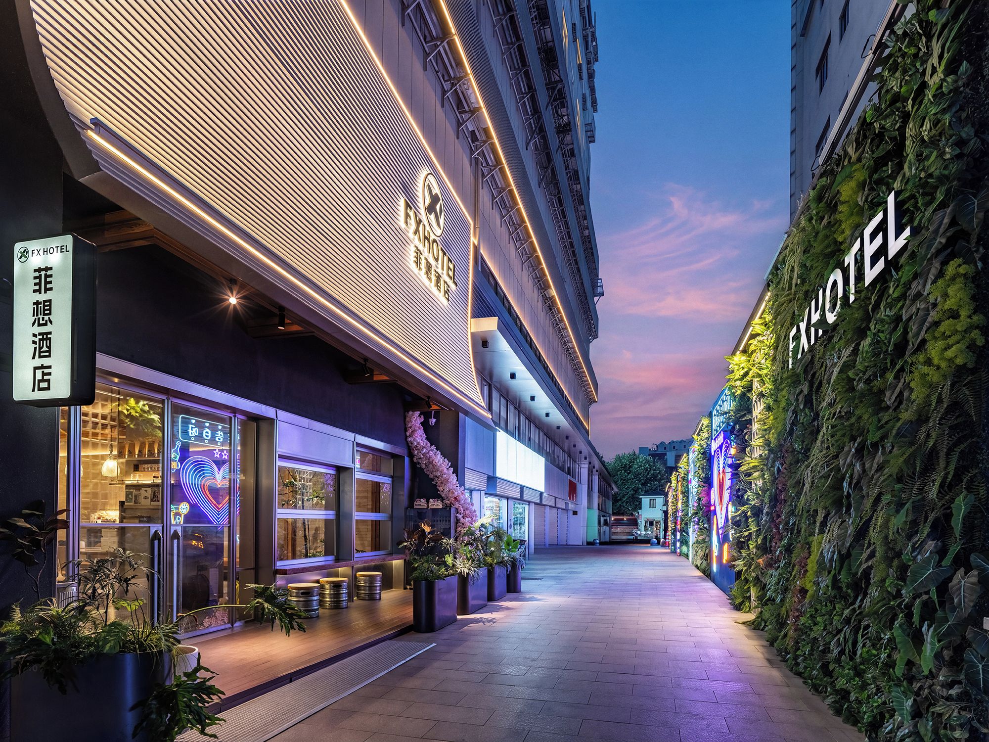 Een hotelgang met een modern ontwerp, met een neonbord en een verticale tuin aan de rechterkant.