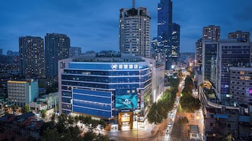A modern hotel with a prominent sign, surrounded by high-rise buildings and a busy street at dusk.