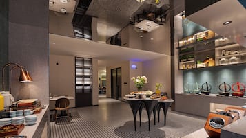 A modern hotel lobby with a central seating area, a reception desk, and a buffet setup.