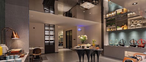 Um saguão de hotel moderno com área de estar central, balcão de recepção e disposição de buffet.