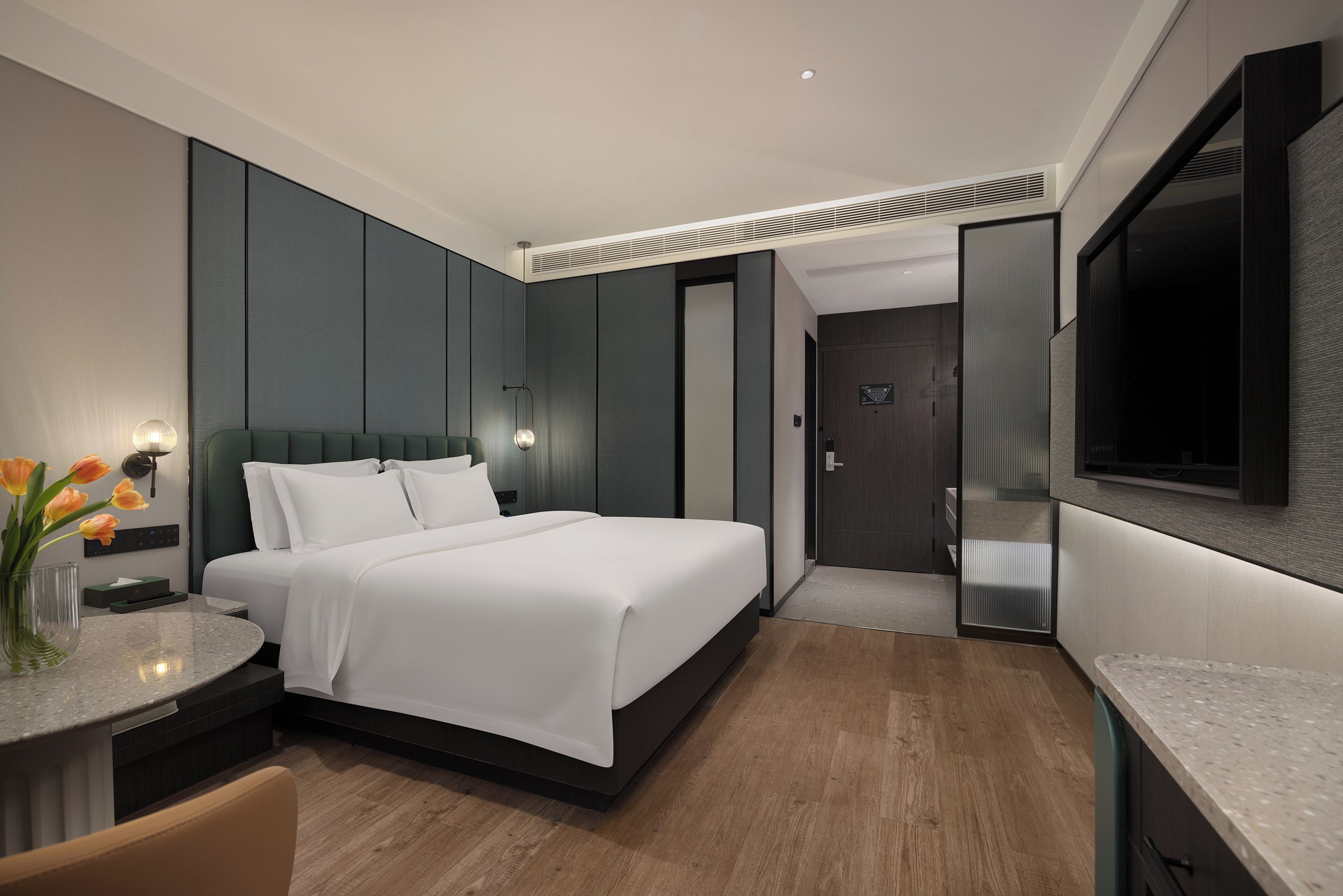 A modern hotel room with a large bed, bedside tables, a desk, and a flat-screen TV.