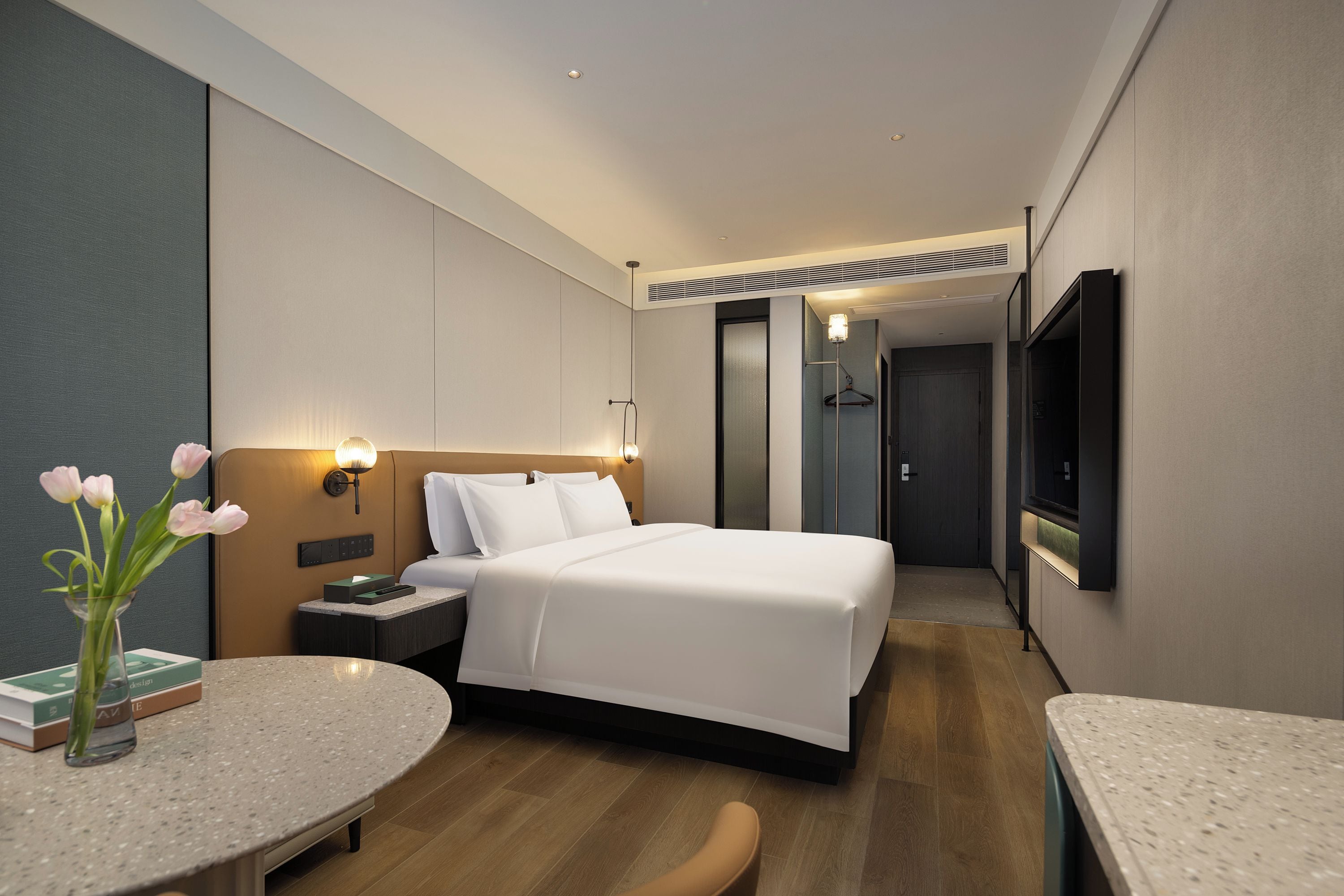 Une chambre d’hôtel moderne équipée d’un lit, de tables de chevet, d’un bureau, d’une chaise, d’une télévision et d’un vase avec des fleurs.