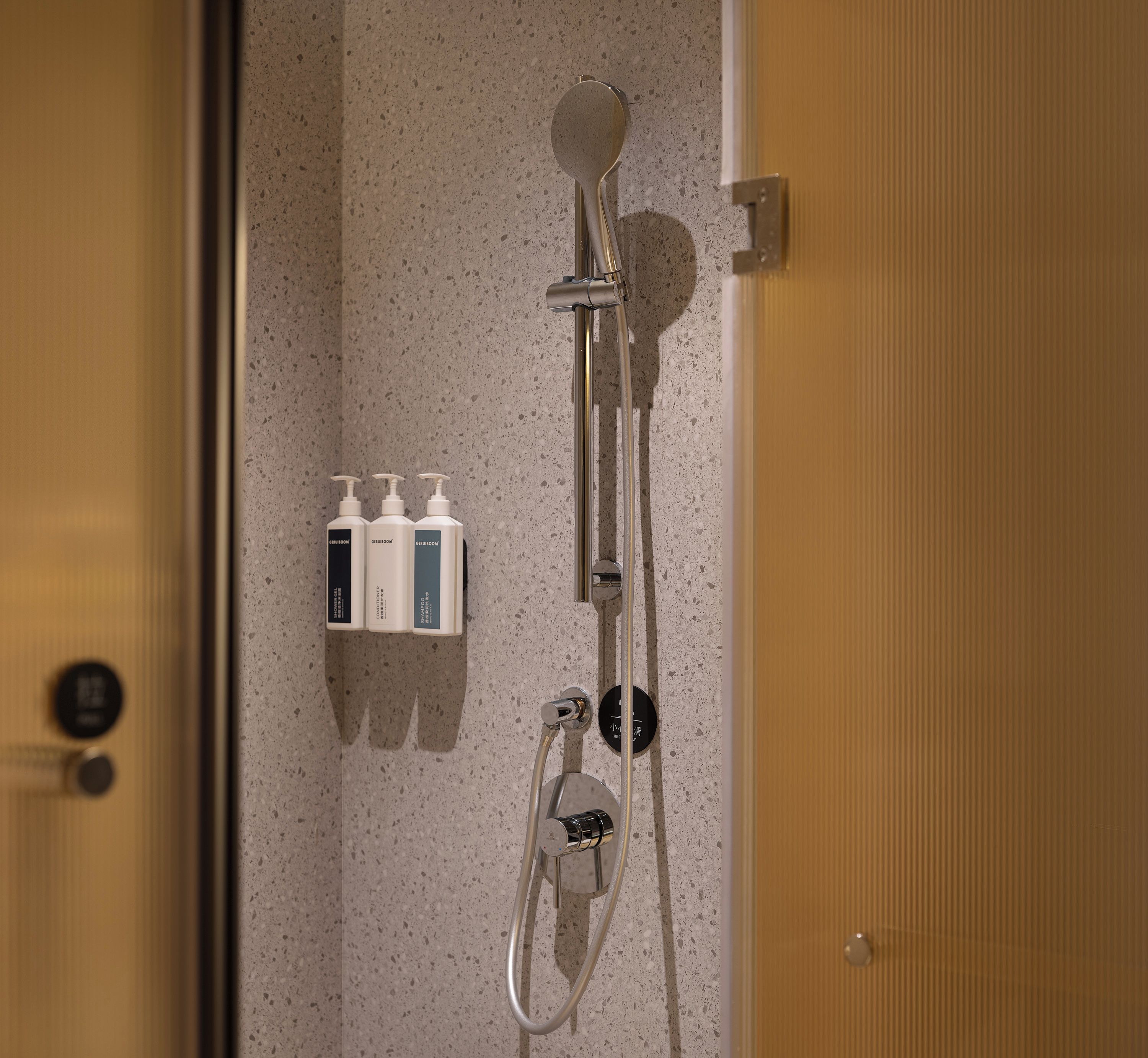 Eine Dusche mit Handbrause, Wandarmatur und zusätzlichen Shampooflaschen an der Wand.