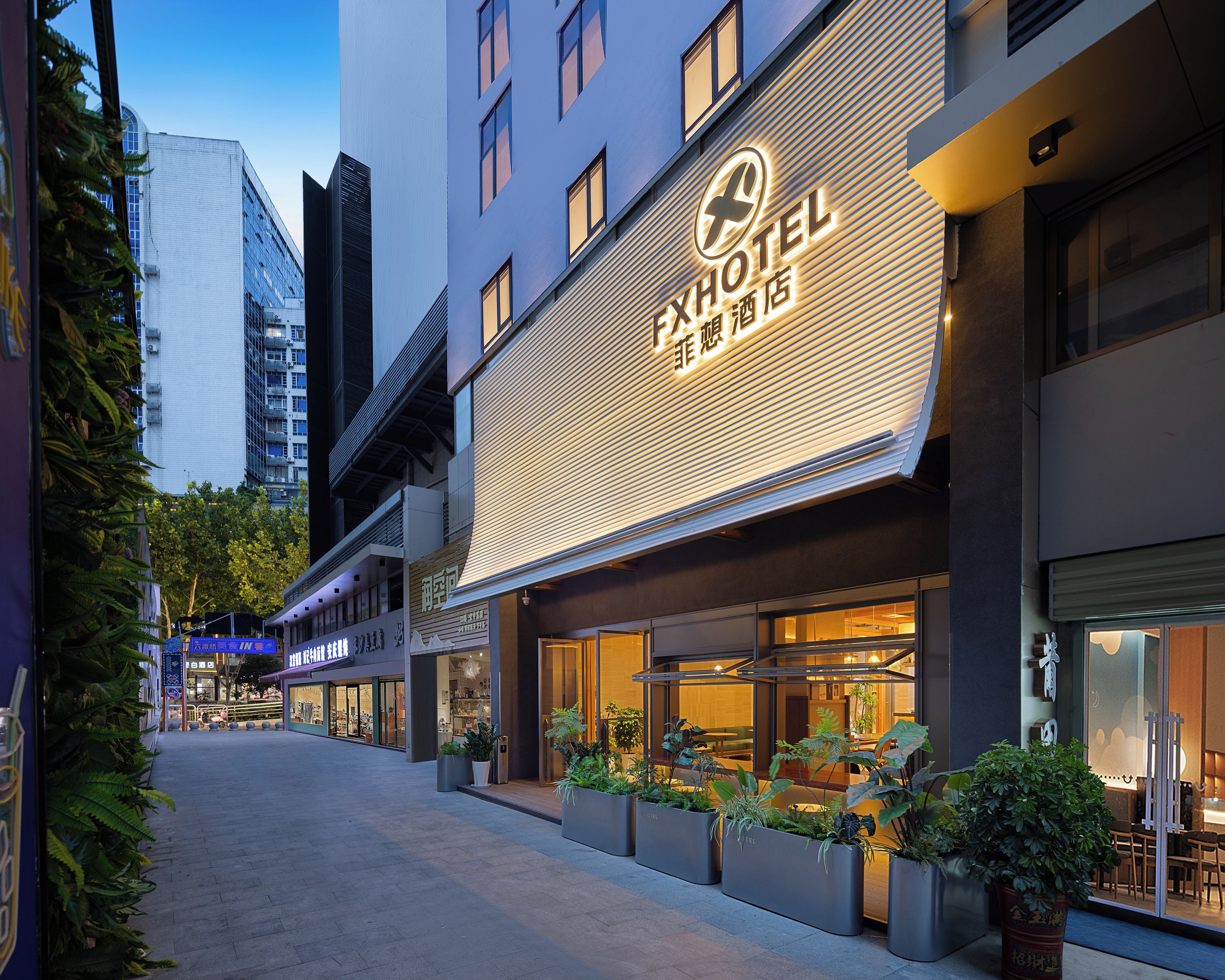 A hotel with a modern facade, large windows, and outdoor seating area with potted plants.