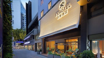 A hotel with a modern facade, large windows, and outdoor seating area with potted plants.