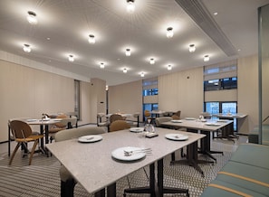 Un salón de conferencias de hotel con varias mesas y sillas, equipado con platos y cubiertos.