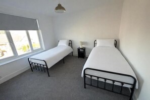 A bedroom with two single beds, a window, and a bedside table with a lamp. - Central Peterborough Home, Garden, Parking, 2 Bed (Peterborough)