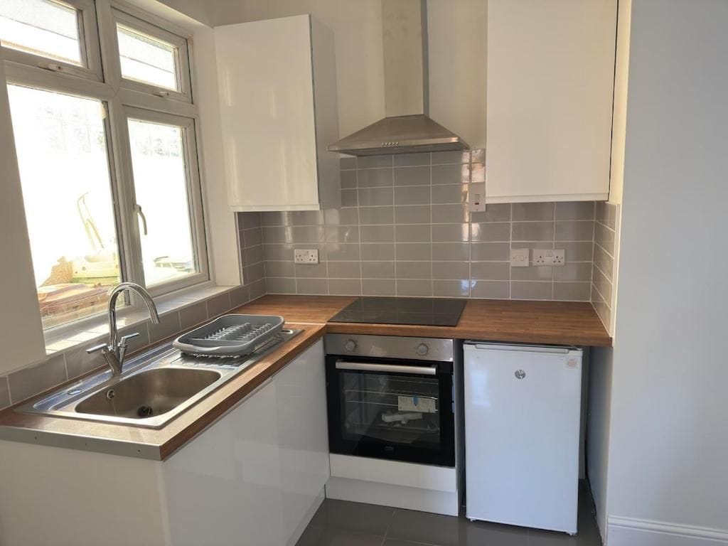 A compact kitchen with a sink, stove, oven, and a small refrigerator.