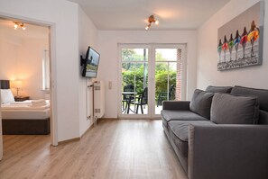 A modern hotel room with a bed, a TV, a sofa, and a dining area with chairs. - Nordlicht Vacation Rental in Büsum: Your Fabulous Vacation by the Sea (Büsum)