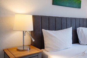 A neatly made bed with white bedding and pillows, a bedside lamp on a wooden nightstand, and a grey upholstered headboard. - Nordlicht Vacation Rental in Büsum: Your Fabulous Vacation by the Sea (Büsum)