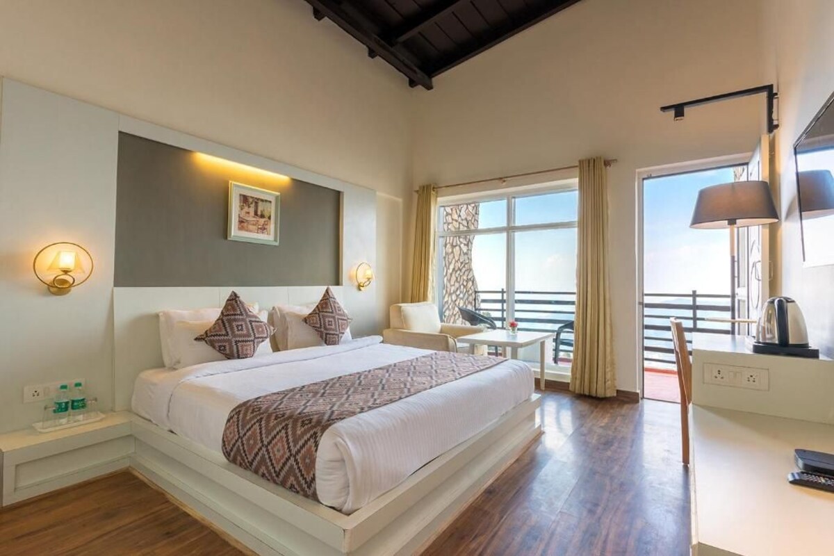 A hotel room with a large bed, bedside lamps, a small table, a chair, and a view of the outside.