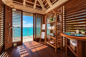 Eine Holzterrasse mit Meerblick, einer Dusche und einem Regal mit Handtüchern und Pflegeprodukten.