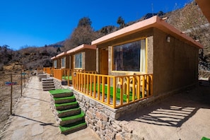 A row of rustic-style cabins with stone foundations and wooden railings, connected by a stone pathway.