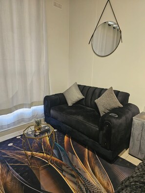 Un salon avec un canapé noir, un miroir rond, une table basse aux motifs géométriques et un tapis à motifs.