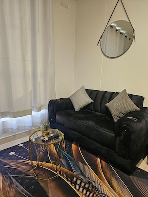 Ein modernes Wohnzimmer mit einem schwarzen Sofa, einem runden Spiegel und einem Glastisch.