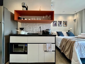 A modern hotel room with a kitchenette, a bed with a view, and artwork on the wall. - Nik Paulista 513 (São Paulo)