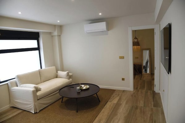A modern living room with a sofa, a round coffee table, and a TV mounted on the wall.