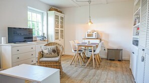 A compact kitchen with a dining area, a television, a microwave, and a wicker chair. - Deichnest Vollerwiek Apartment: A Relaxing Getaway by the Sea (Vollerwiek)