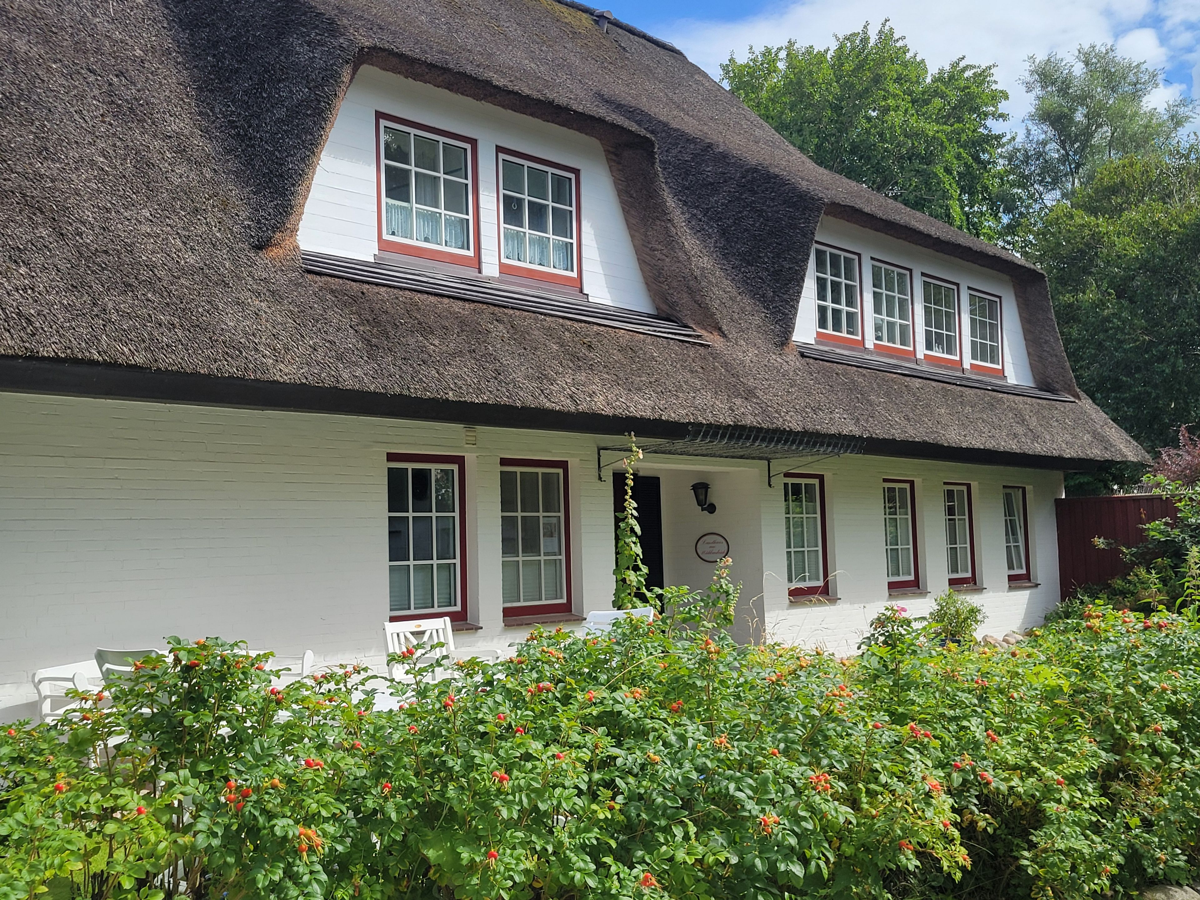 A traditional house with a thatched roof, white walls, and red window frames.