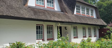 Une maison traditionnelle avec un toit de chaume, des murs blancs et des encadrements de fenêtres rouges.