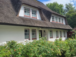 A traditional house with a thatched roof, white walls, and red window frames. - Deichnest Vollerwiek Apartment: A Relaxing Getaway by the Sea (Vollerwiek)