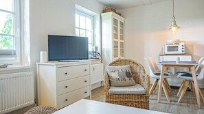 A modern kitchen with a television, white cabinetry, a wicker chair, and a dining table with chairs. - Deichnest Vollerwiek Apartment: A Relaxing Getaway by the Sea (Vollerwiek)