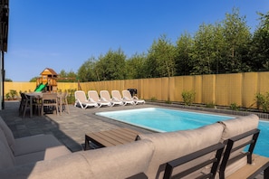 A backyard with a swimming pool, lounge chairs, a wooden deck, and a play structure. - Spacious 5-bedroom house with jacuzzi, sauna and pool (Mielno)