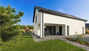 Una casa moderna a un piano con veranda coperta, un'area giochi sullo sfondo e un prato curato.