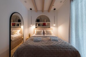 Una camera da letto con un letto grande, due comodini, uno specchio e una mensola con libri e oggetti decorativi.