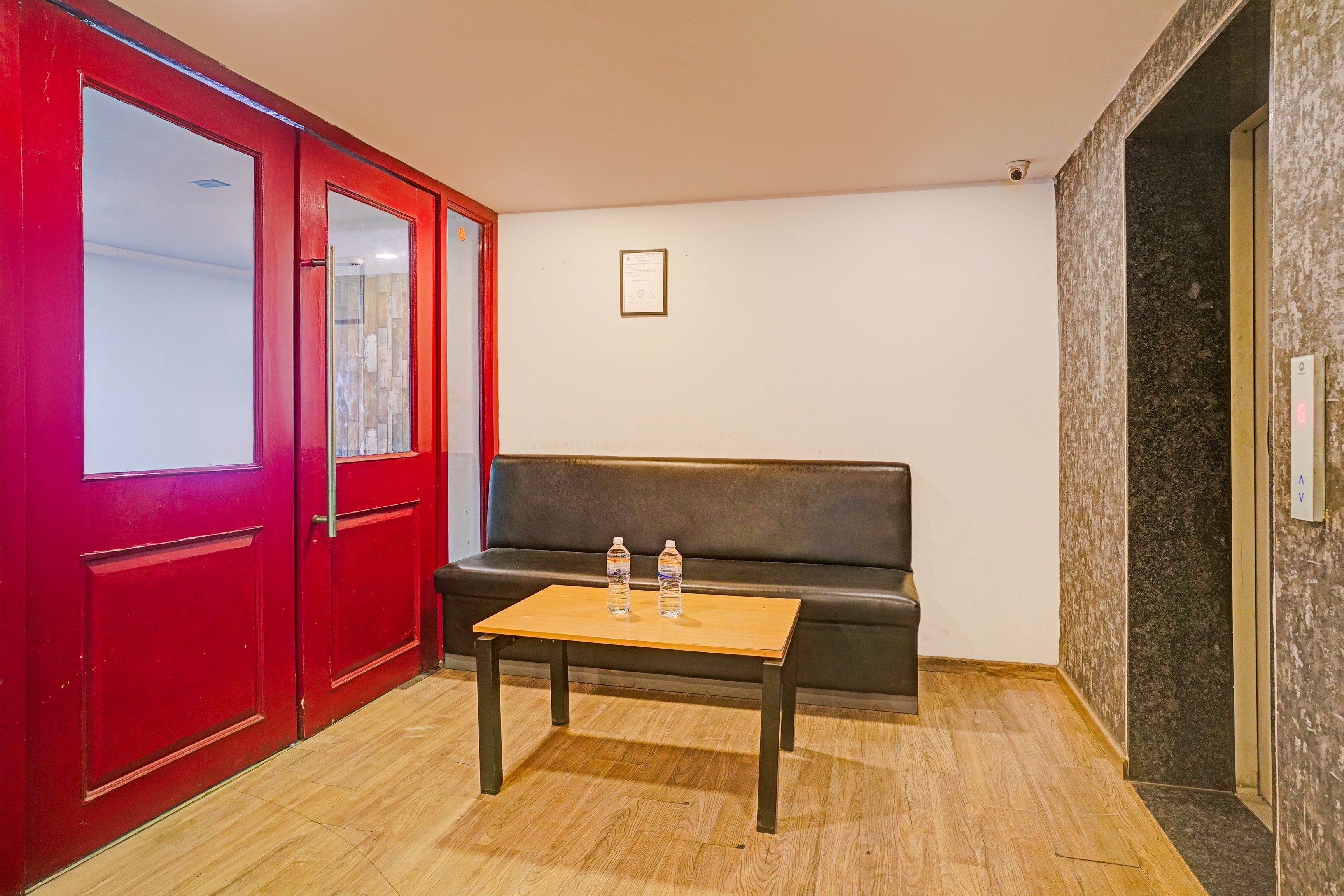 Una habitación con una puerta roja, un sofá negro y una pequeña mesa con dos botellas de agua.