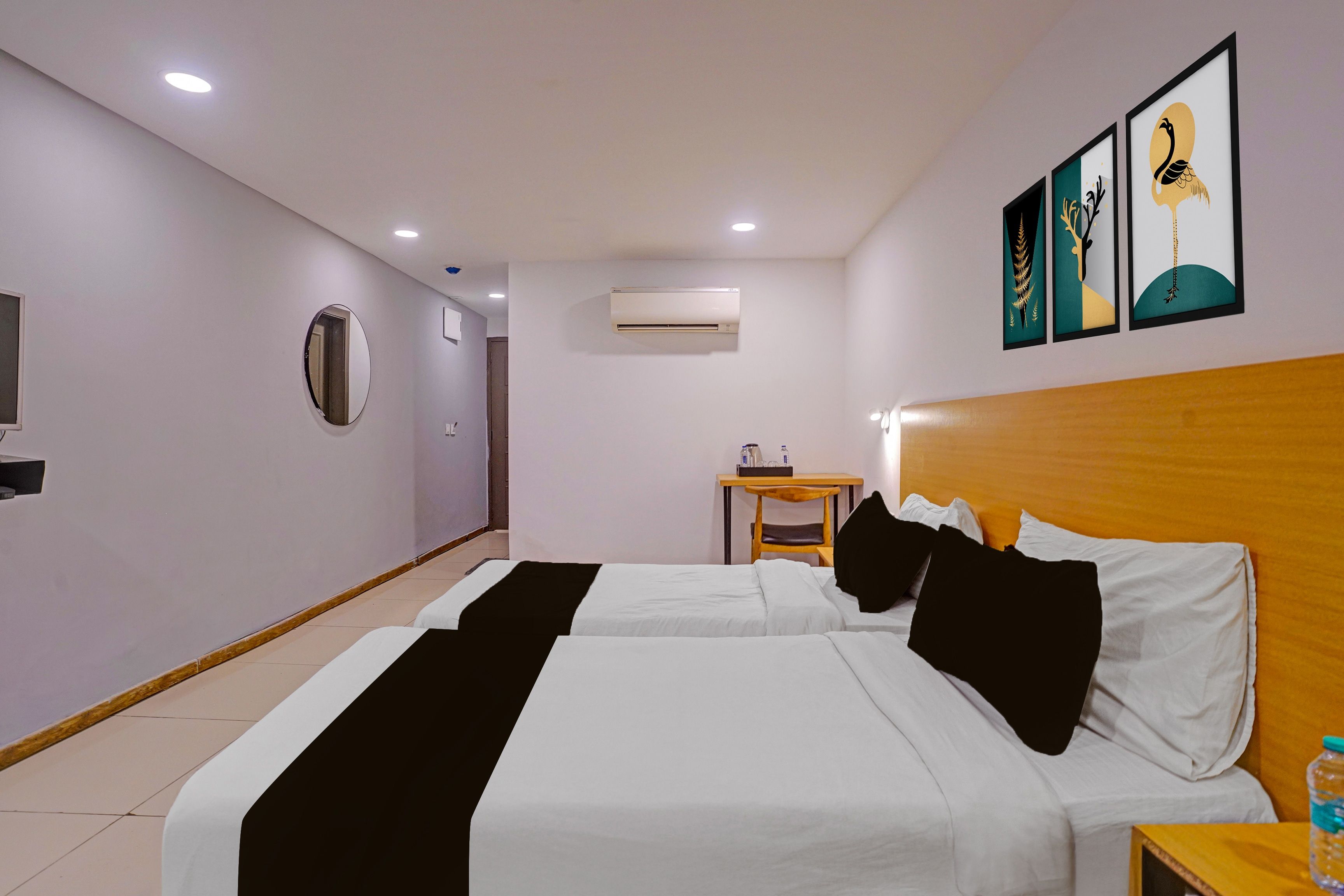 Une chambre d’hôtel avec deux lits, une tête de lit en bois, une petite table, une chaise, un appareil de climatisation et des œuvres d’art accrochées au mur.