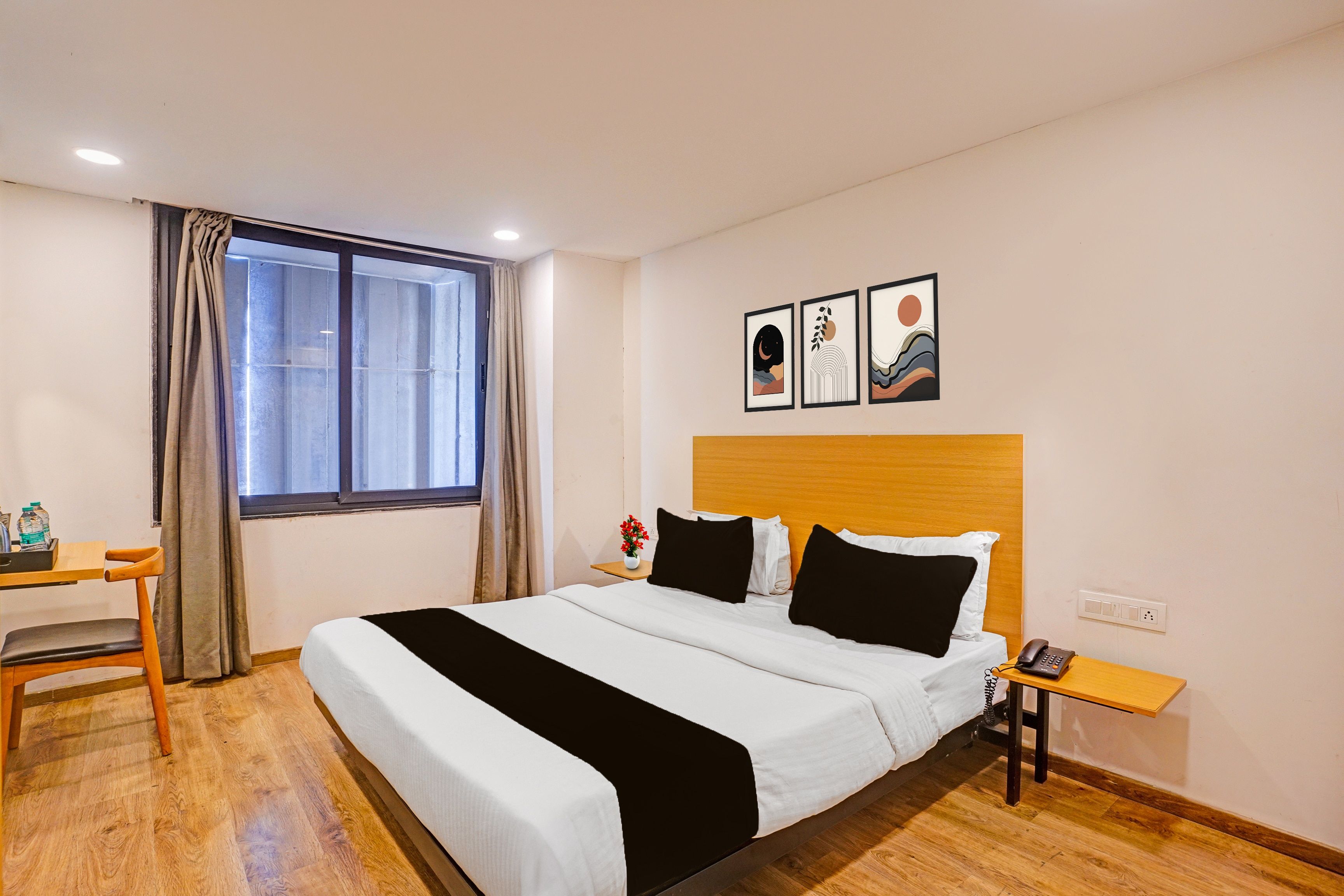 Habitación de hotel con cama, mesita de noche, escritorio con silla, ventana con cortinas y decoración en la pared.