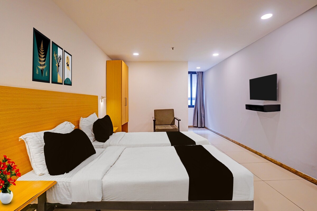 A hotel room with two beds, a TV mounted on the wall, and a window with curtains.