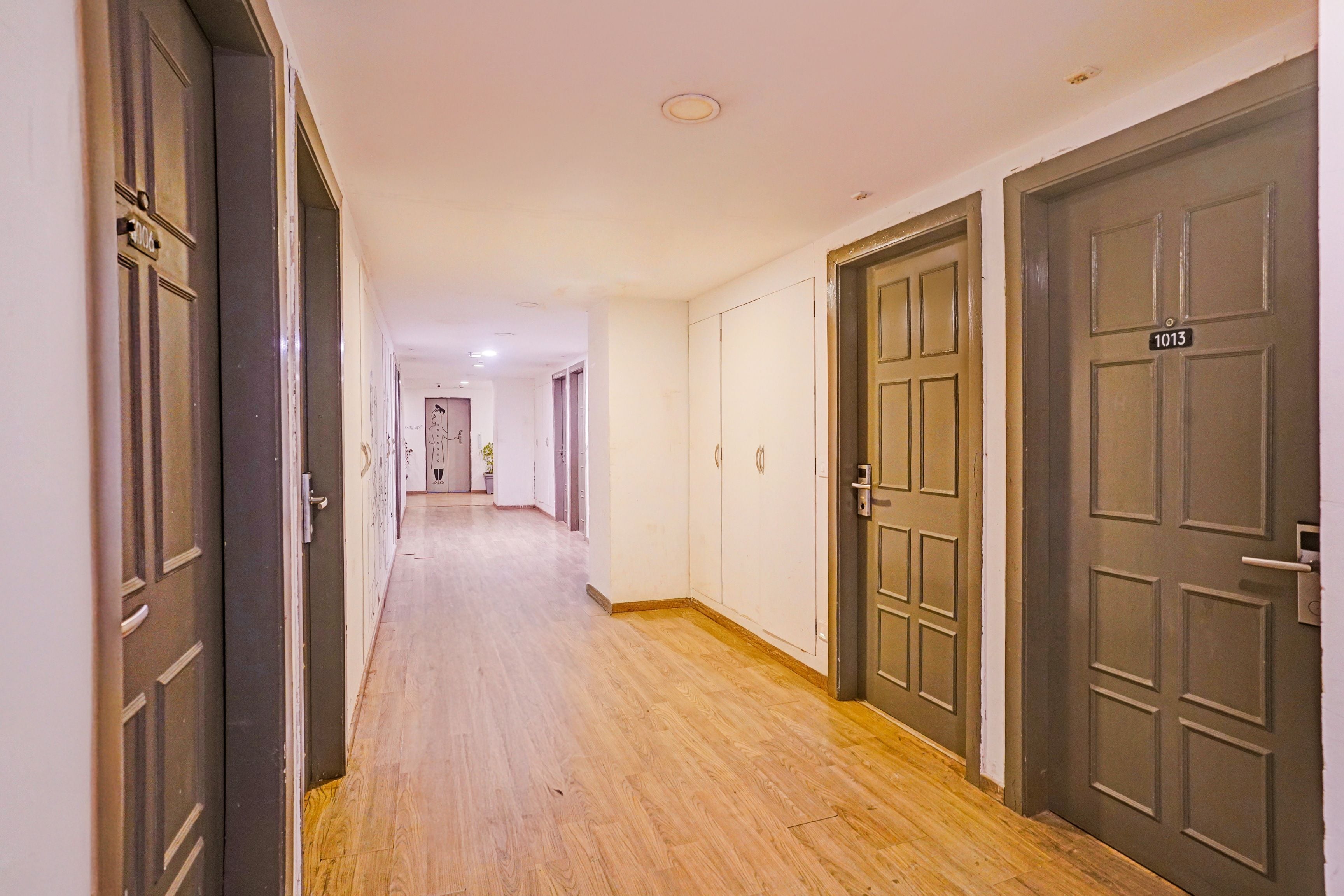 Un pasillo con suelo de madera, puertas a ambos lados y techo con iluminación empotrada.