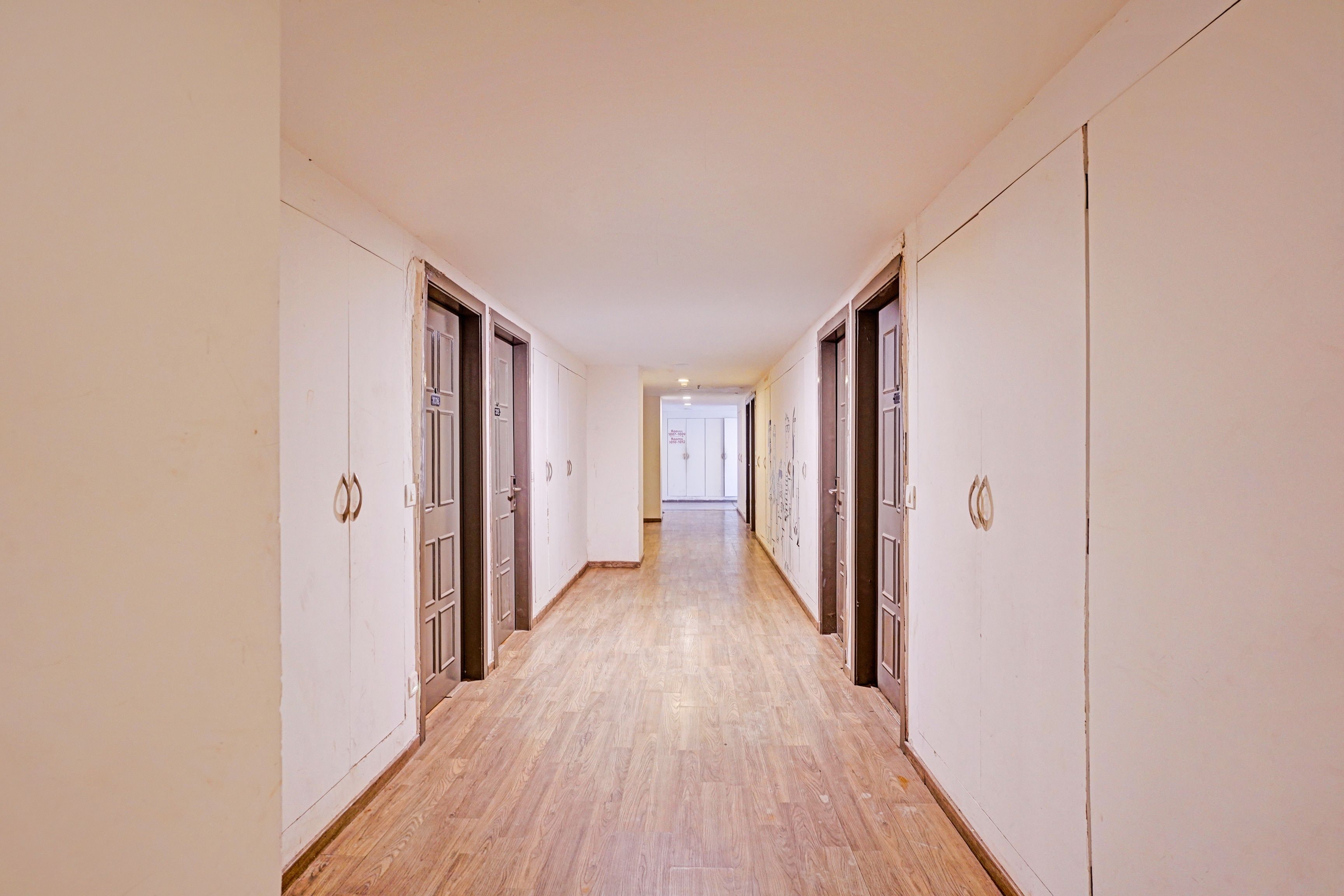 Un pasillo largo y estrecho con piso de madera y paredes blancas, que conduce a una puerta al final.