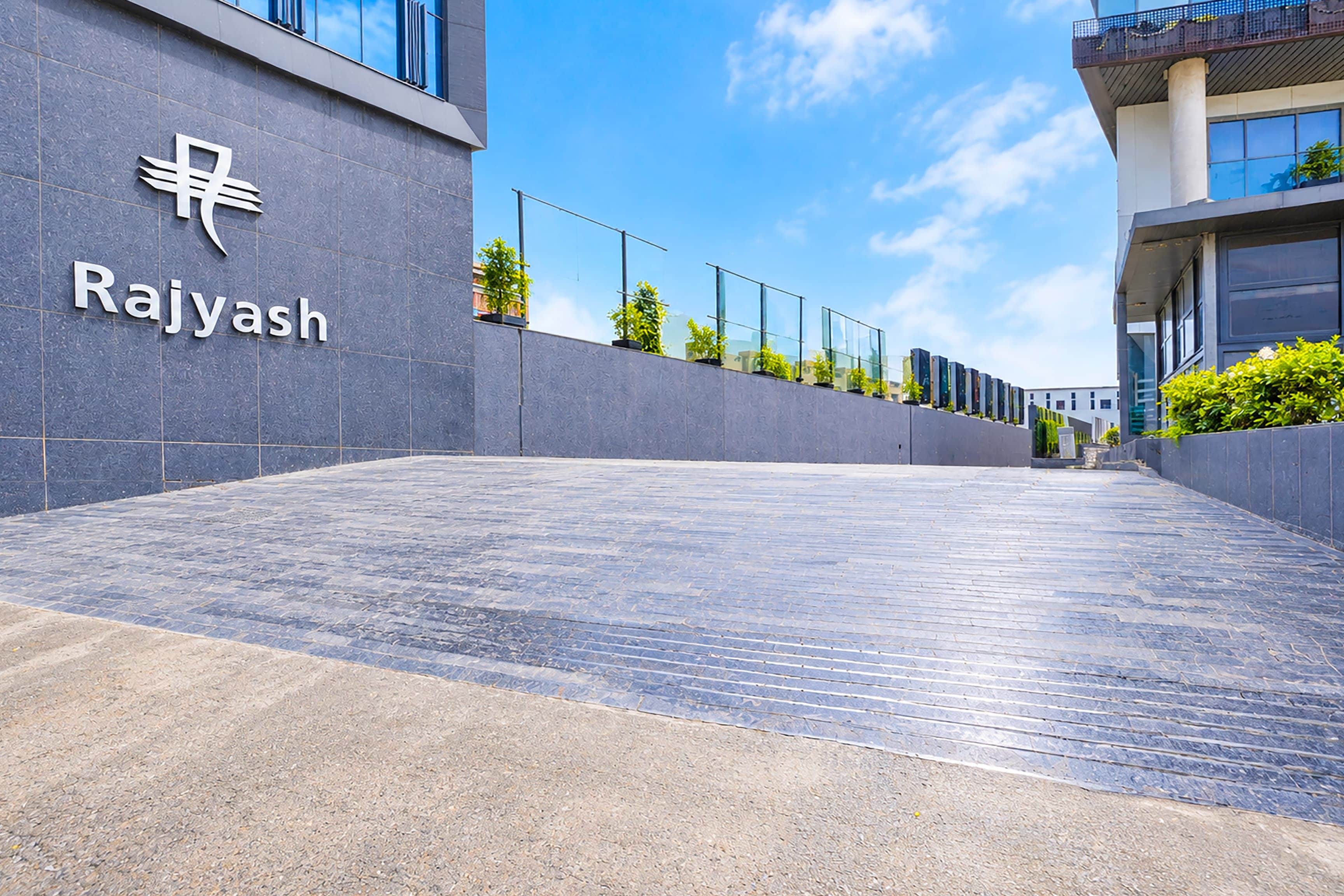 Entrada moderna de un edificio con un letrero que dice 'Rajyash' y un camino pavimentado que conduce a la entrada.