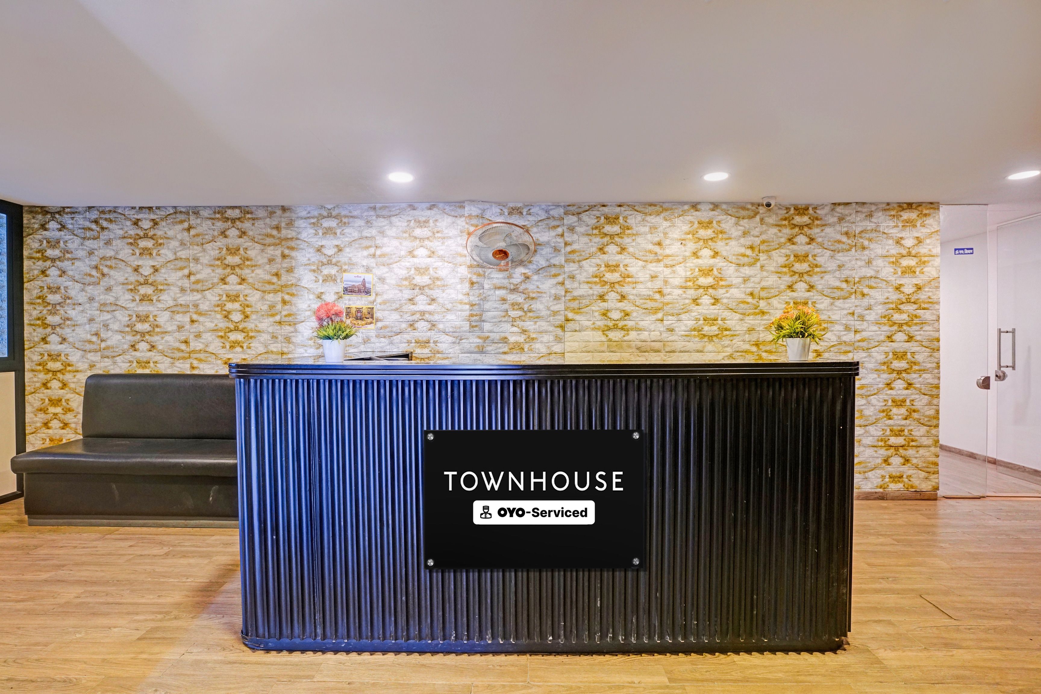 A reception desk labeled 'TOWNHOUSE' with a 'YO-Serviced' sign, a grey sofa, and patterned wallpaper.